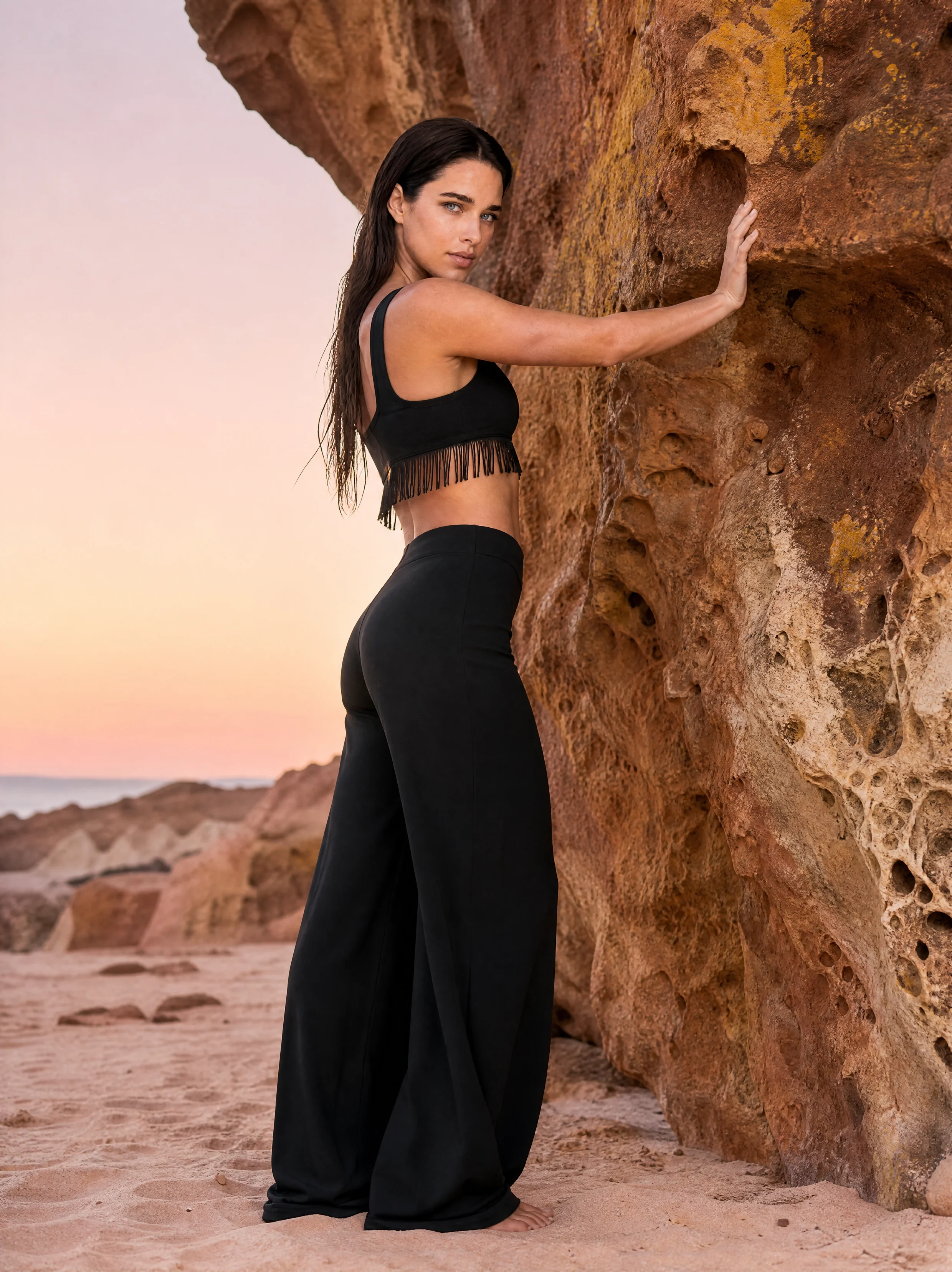 Anna Volkowa – Frau in schwarzem Top und weiter Hose an einer roten Felswand am Meer