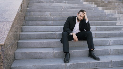 Man in suit sitting on outdoor stairs looking down illustrating the Failed French Language Test for Citizenship
