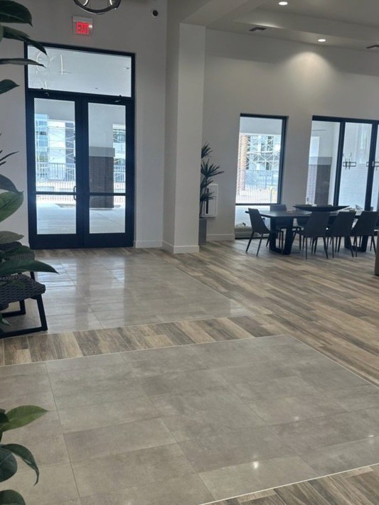 Modern open-plan living area with wood-look tile flooring, large windows, and dining area in a new home under construction.