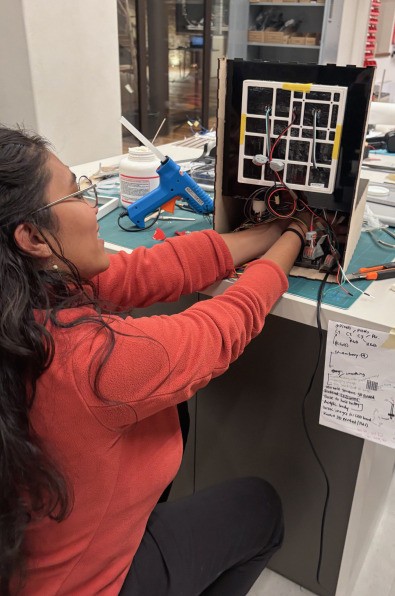 A person wires a gridded LED panel inside a black box at a workbench