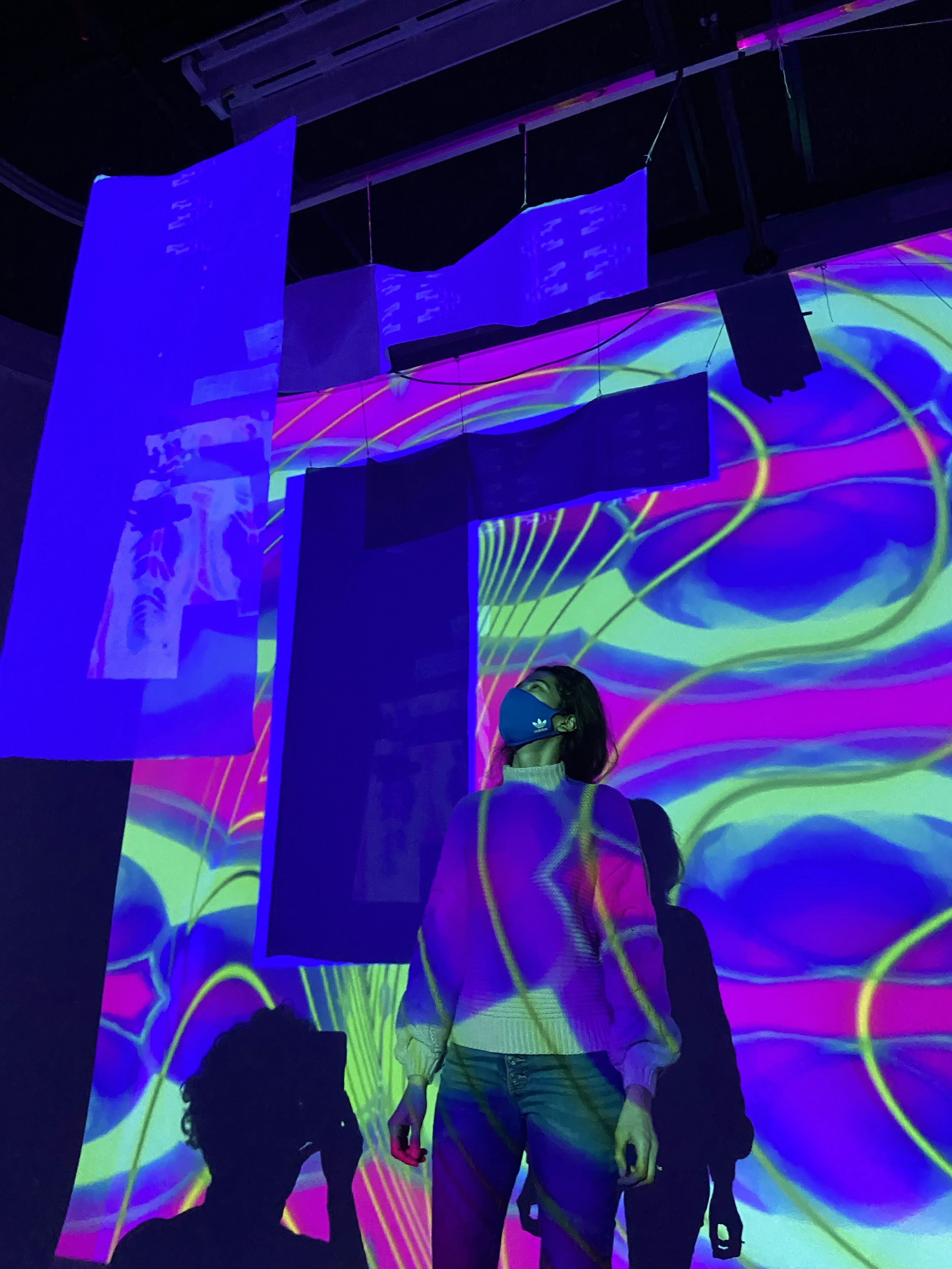 An audience member stands among suspended projection screens surrounded by responsive psychedelic visuals.