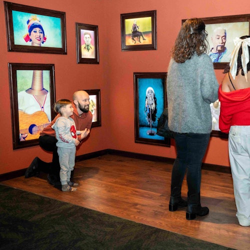 三位成年人和一位小孩在一家橙色墙壁和木质地板的艺术画廊中欣赏别具一格的肖像画。