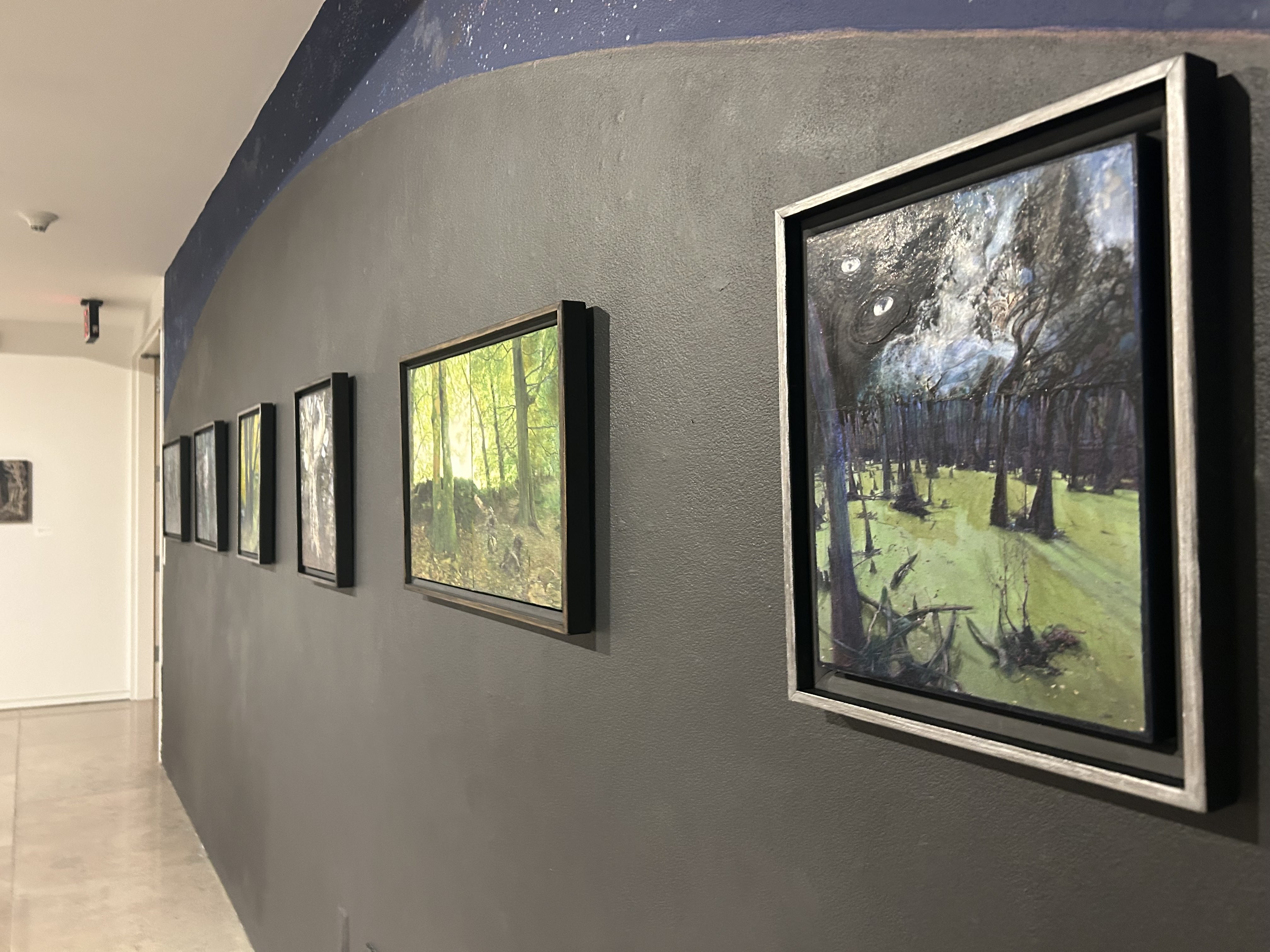 Several paintings hung over a mural of a planet in the night sky