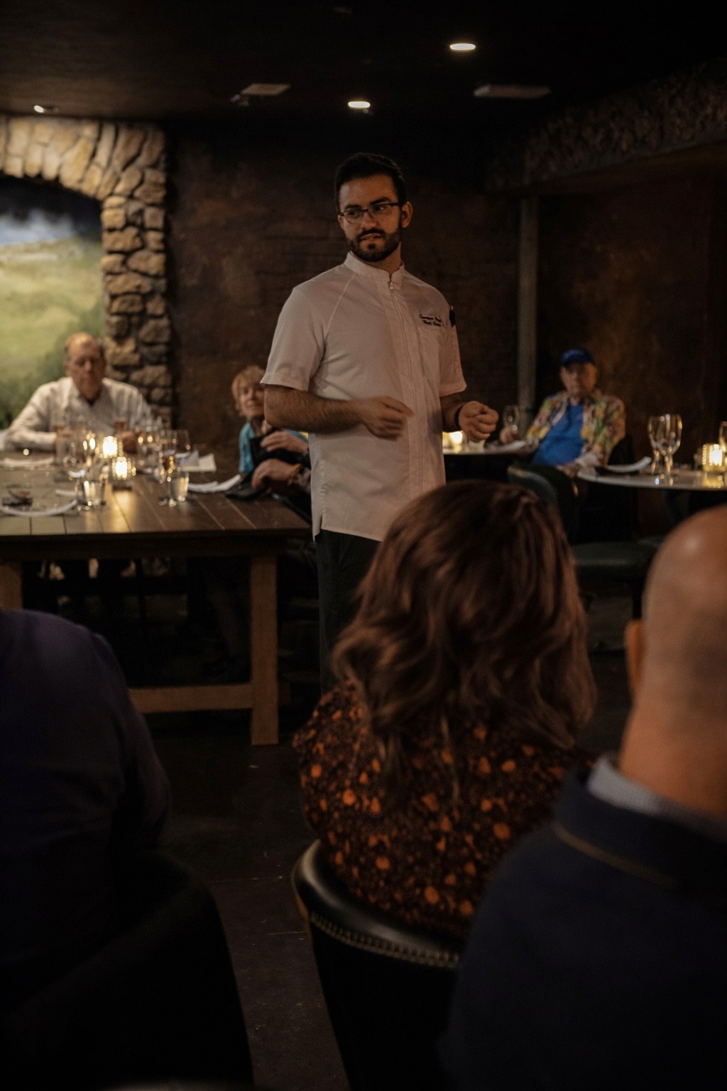 A chef speaking to guests seated at a dinner in the Cellar