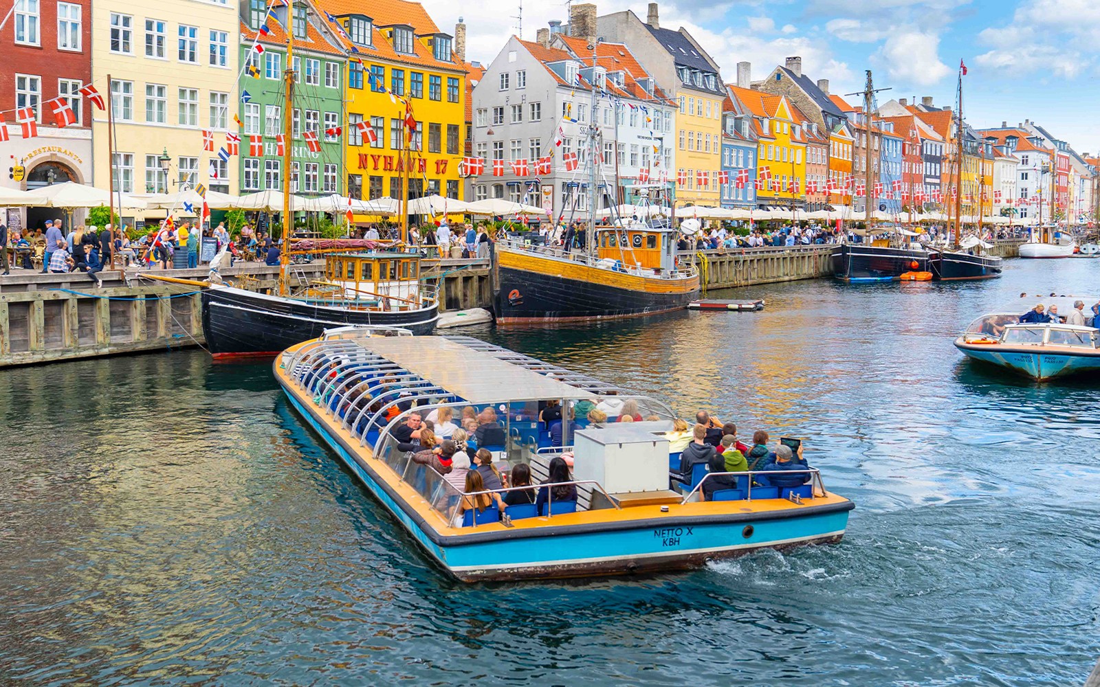 Csatorna túrahajó Nyhavnban, Koppenhágában, elhalad a színes épületek és kikötött hajók mellett.