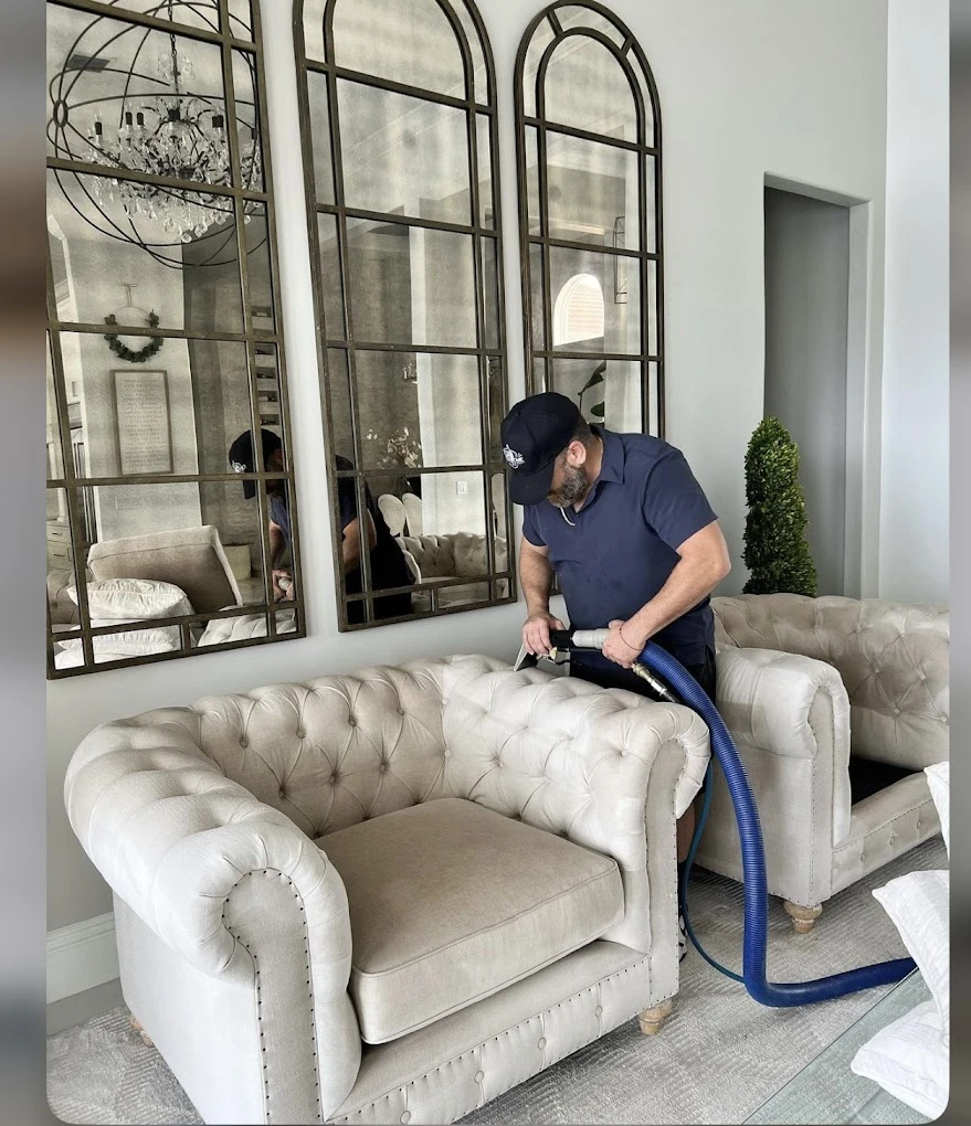 Hombre limpiando un sillón beige con una aspiradora en una elegante sala de estar.