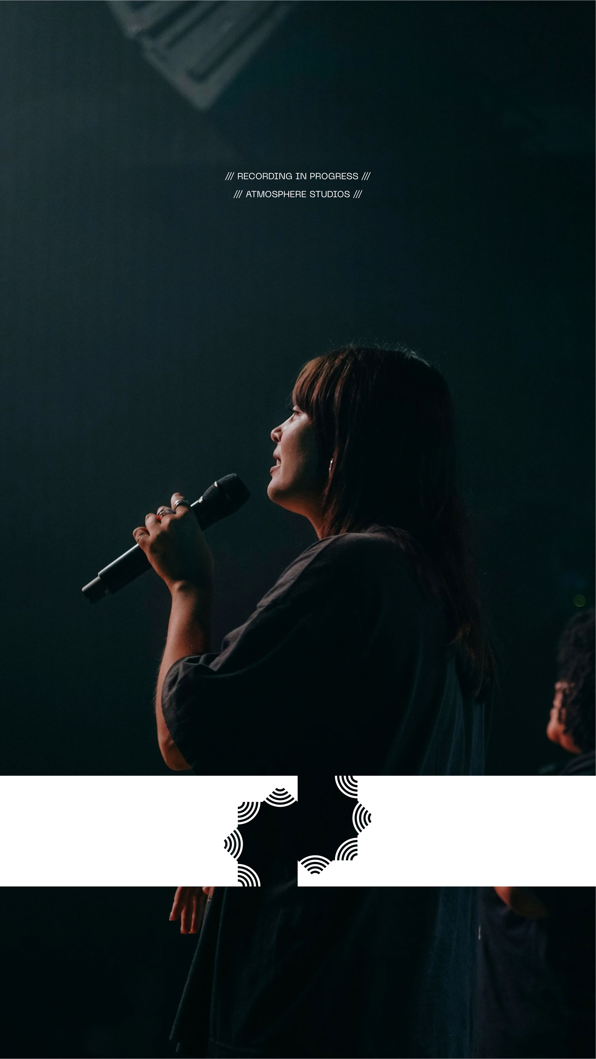 A woman sings into a microphone on a dimly lit stage, creating an intimate and atmospheric music performance scene.