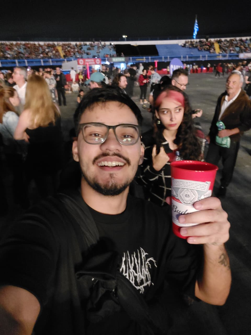 Pessoa tirando selfie em show noturno, com público e arquibancada ao fundo