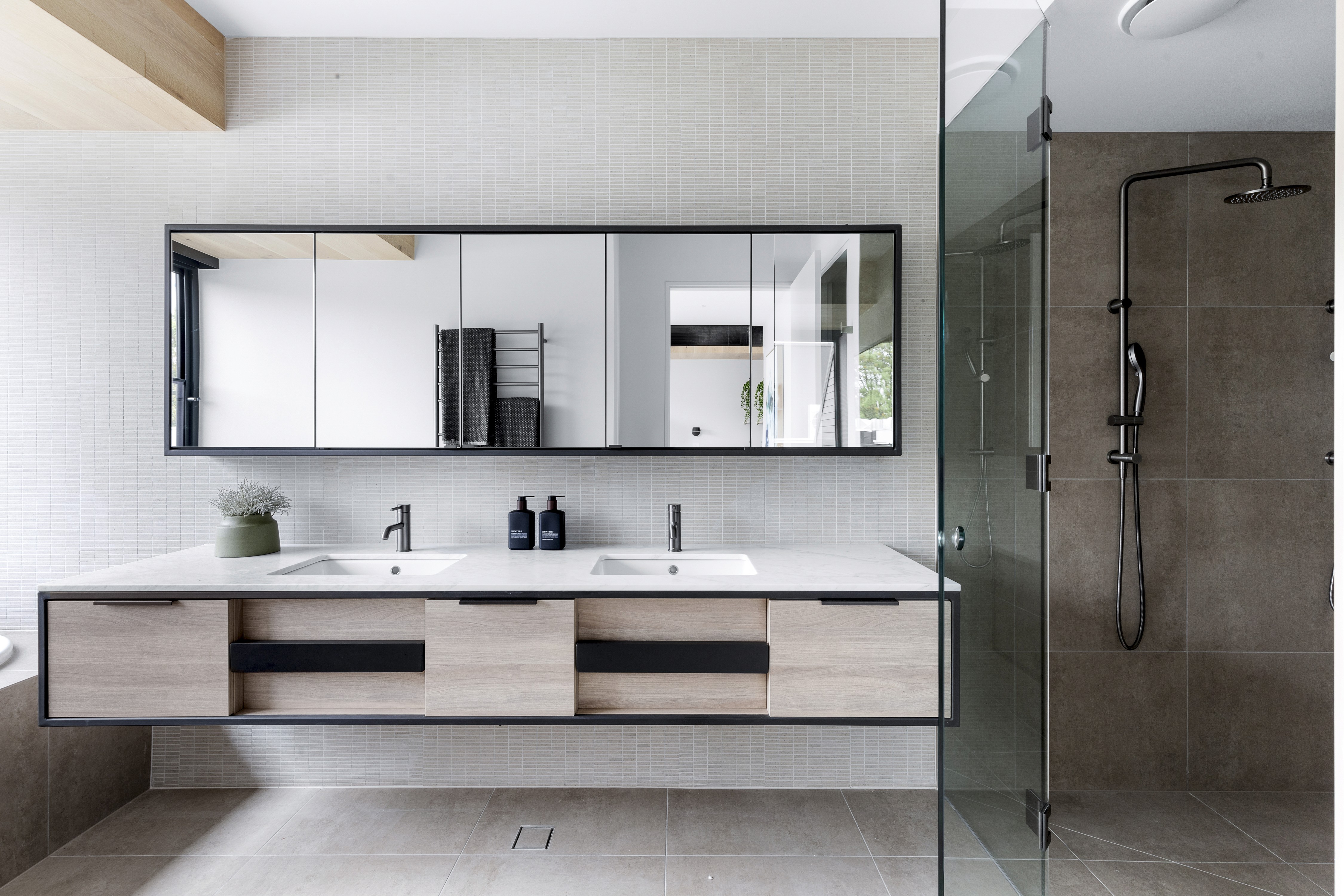 Modern bathroom with double sinks, glass shower, and stylish vanity.