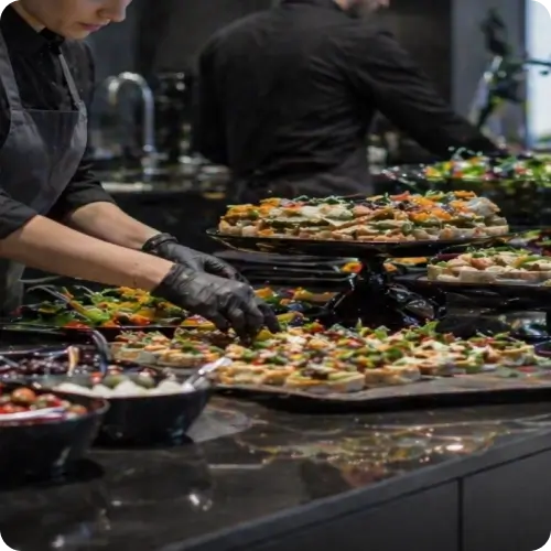Equipe de catering preparando finger foods para evento empresarial de grande porte em operação profissional e organizada.