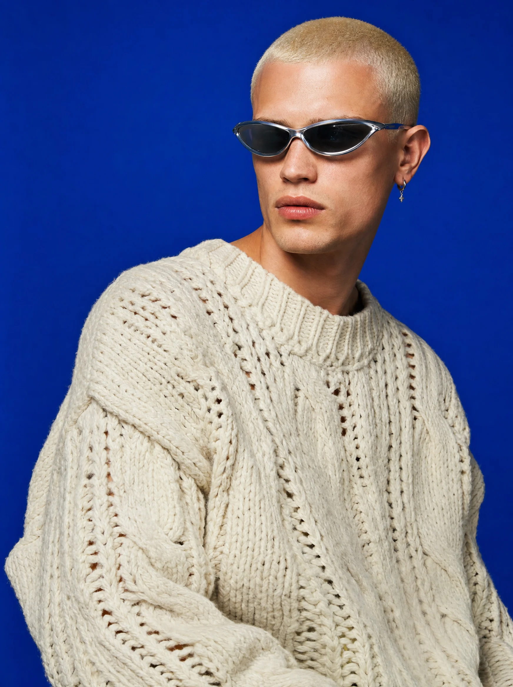 Man in a cream cable-knit sweater and sunglasses against cobalt blue, from the Blanc Studio lookbook