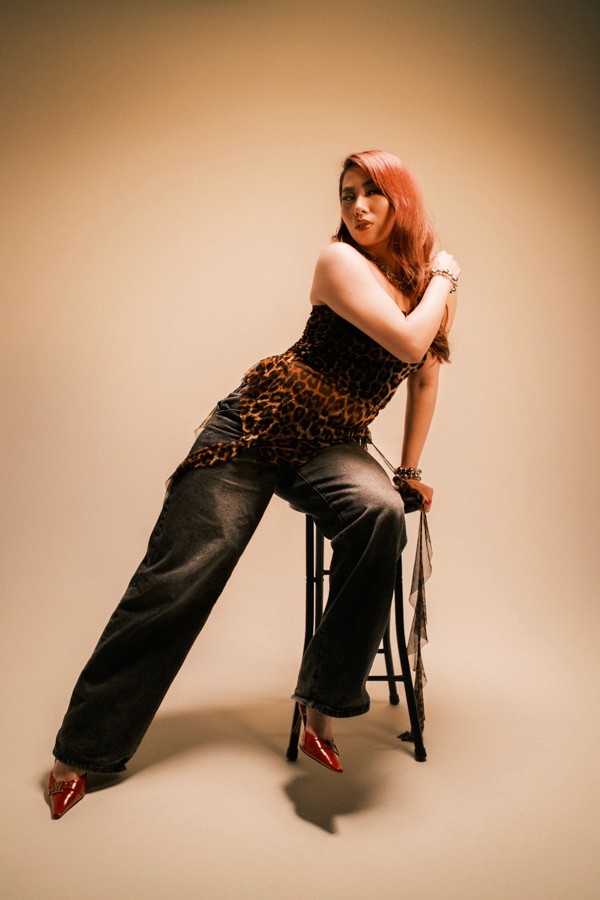 Red-haired model standing beside a stool under warm light
