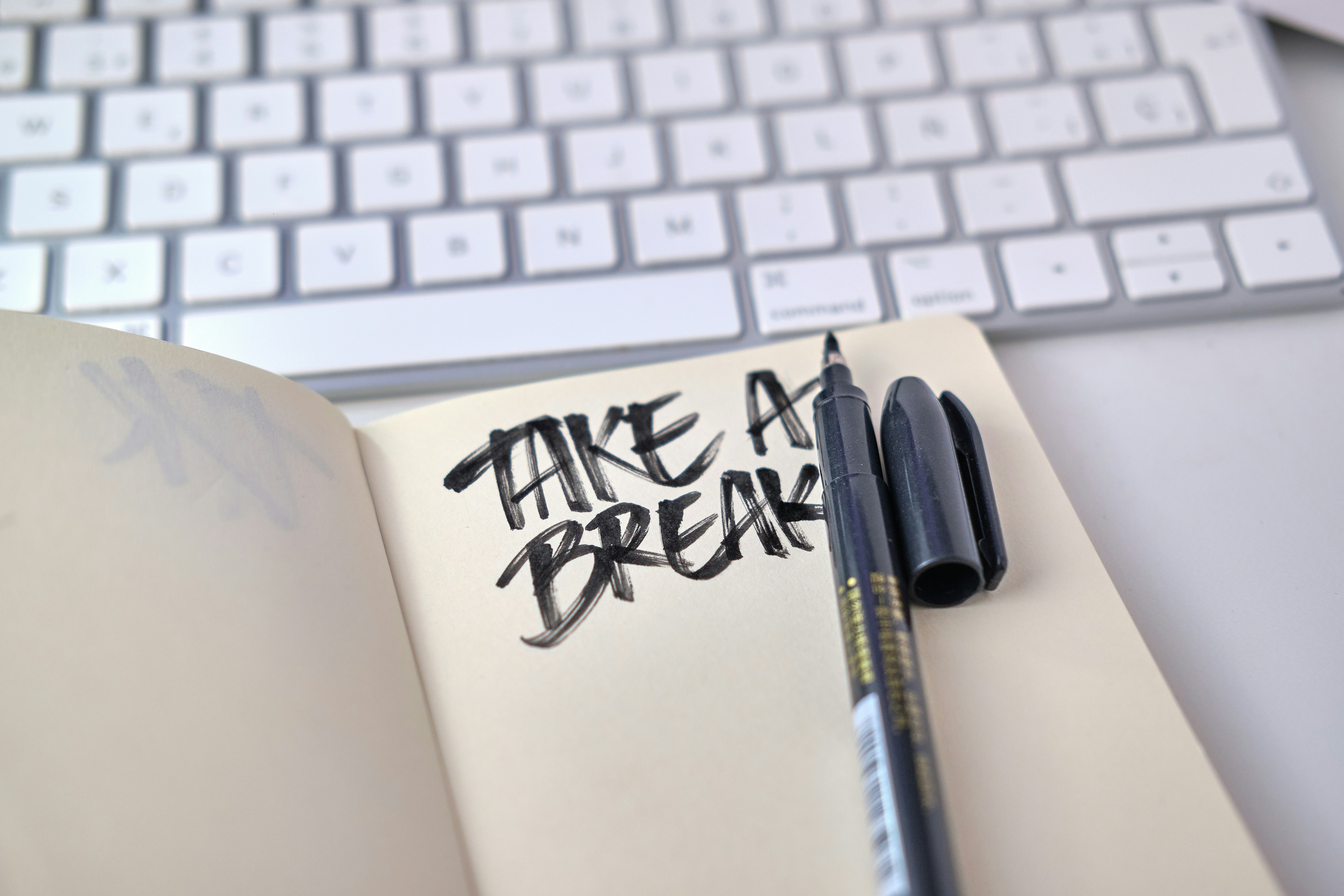 An open notebook with "Take a break" written in bold letters and a black pen on a desk with a keyboard in the background
