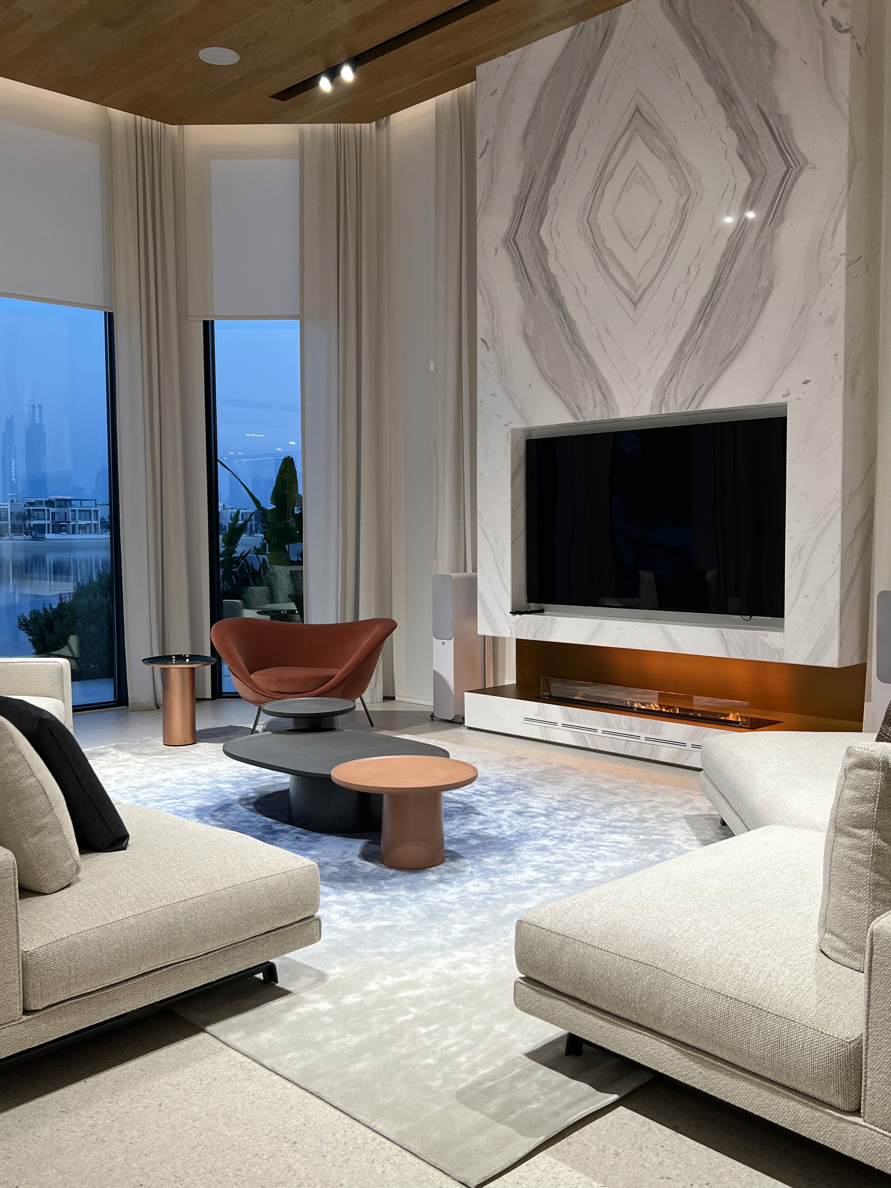 A softly lit hallway with a series of arched doorways, warm-toned walls, and wood flooring leading toward a seating area with neutral furniture.