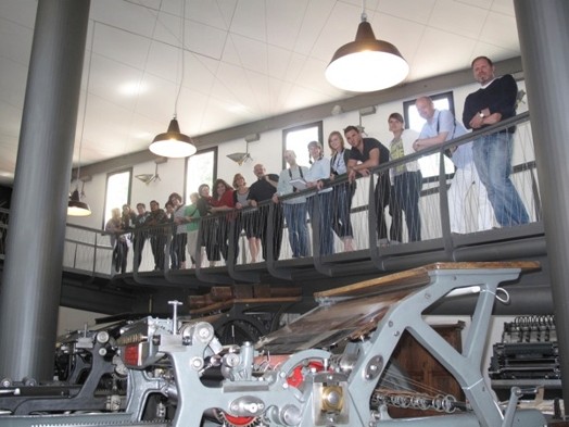 A photo of a group of people looking at some printing presses.