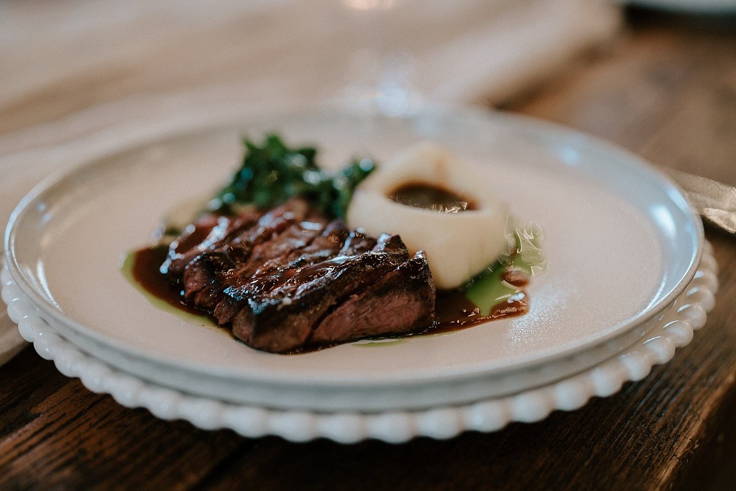 Close-up of a seared steak with mashed potatoes and greens served on a decorative plate.