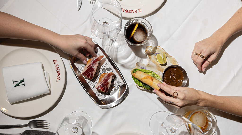 White plate with roasted chicken served in a golden sauce with herbs and capers, placed on a terrazzo tabletop in sunlight.
