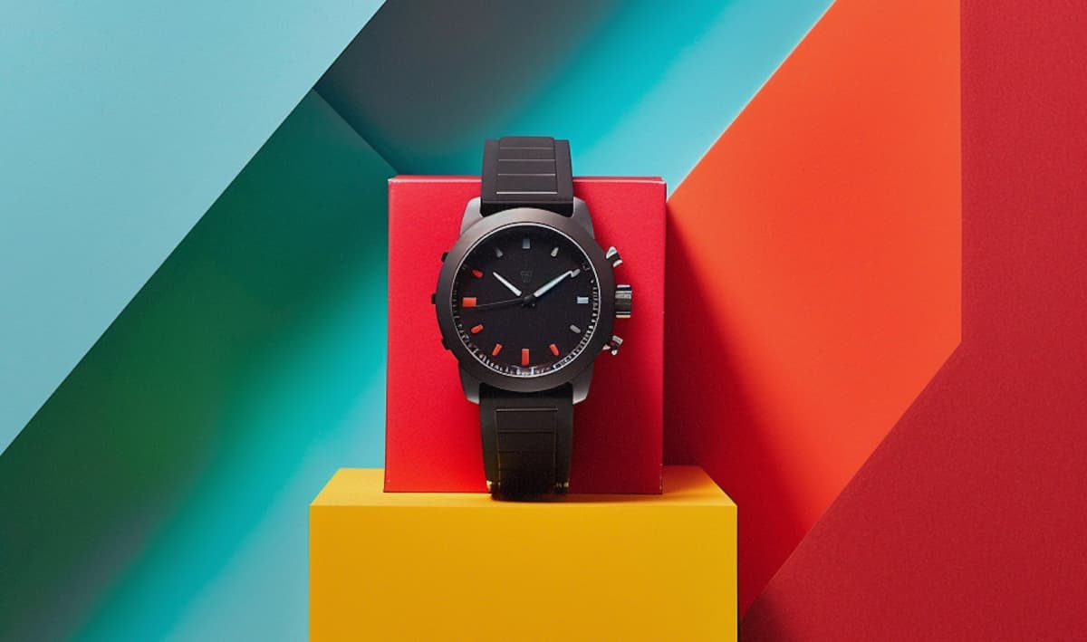 A black sportswatch displayed against a blue, red and yellow geometric background