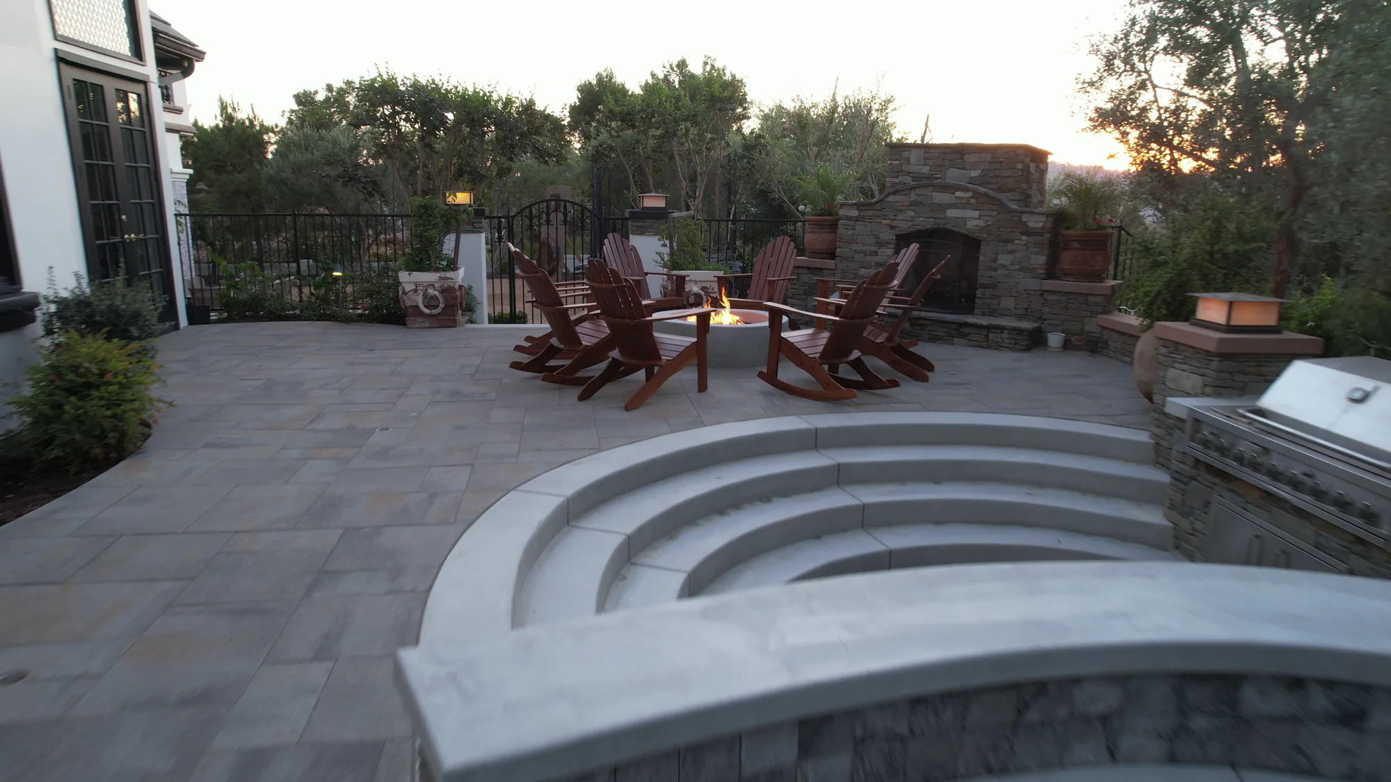 Curved pale steps lead from the pool edge to the paved fire bowl seating area.