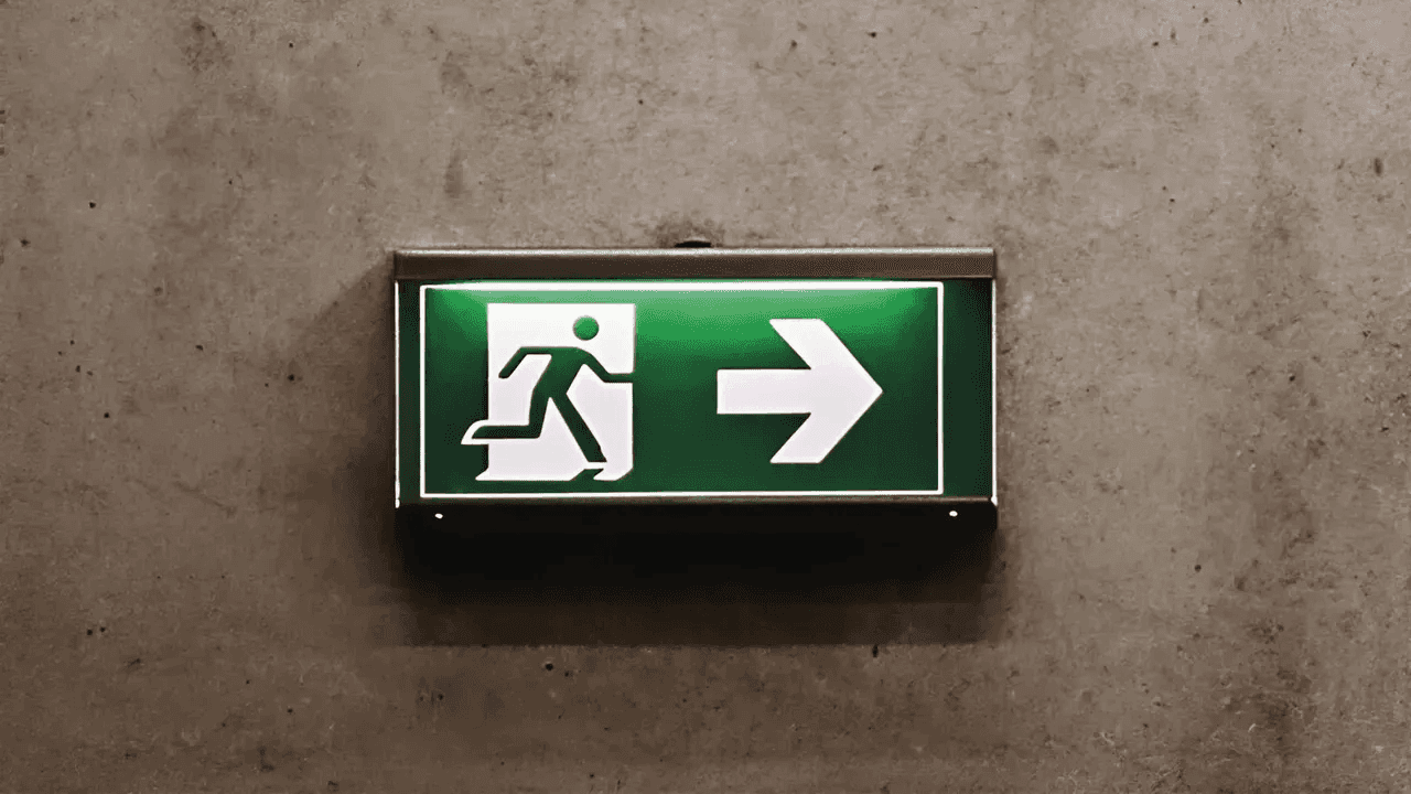 Illuminated green exit sign pointing right on concrete wall.