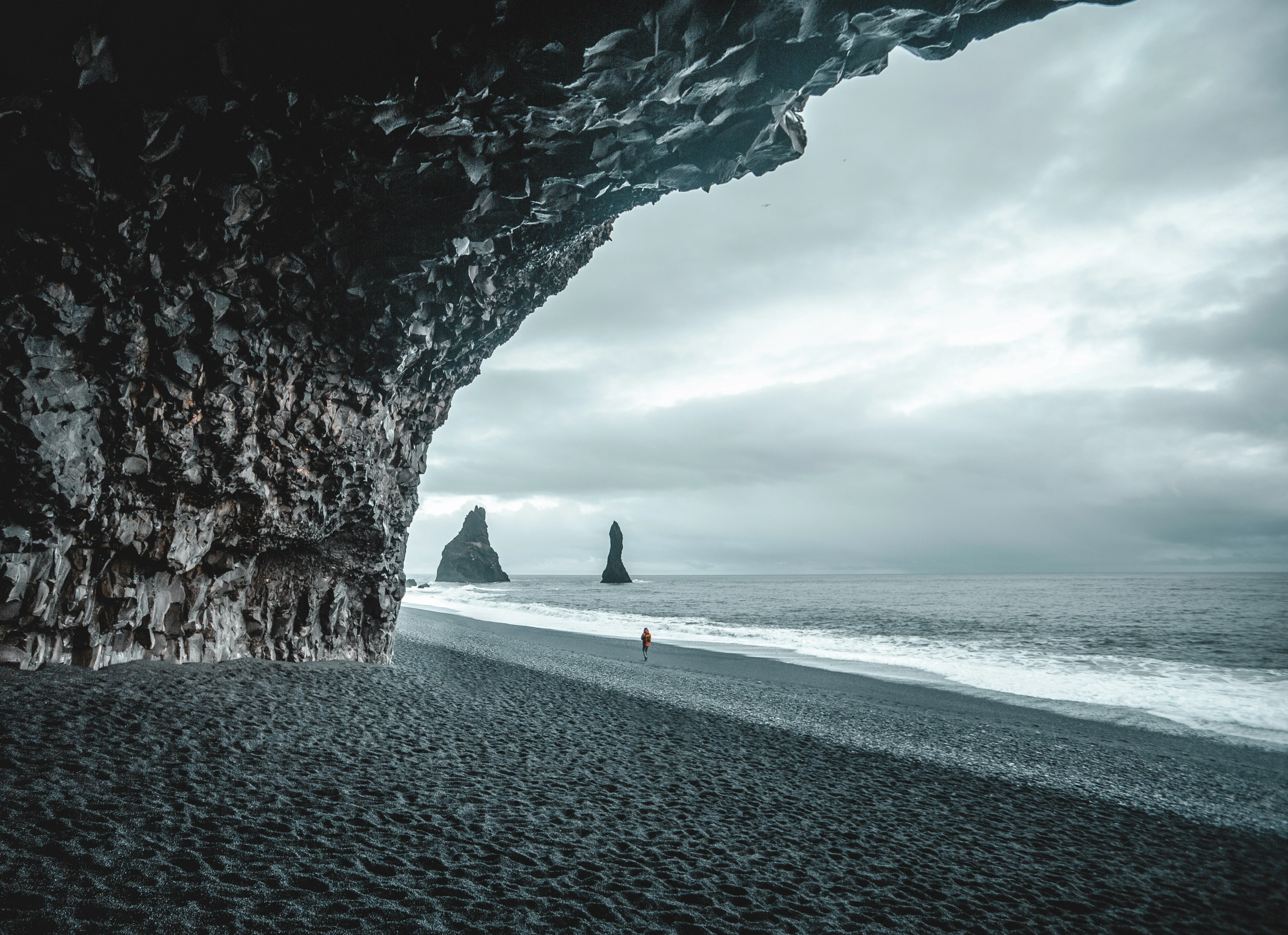 View from inside a basalt column cave on a black sand beach, looking out at sea stacks rising from the ocean.