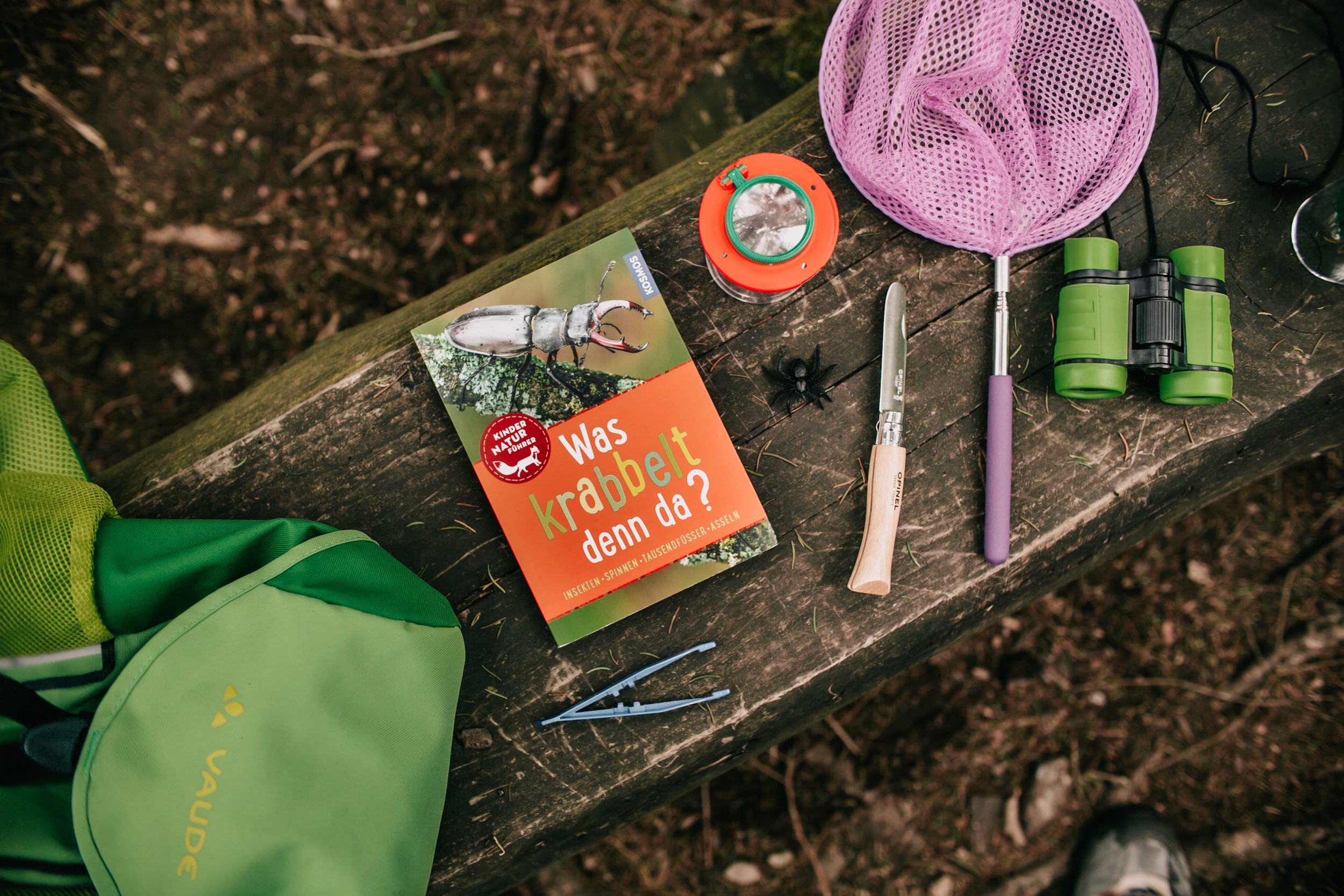 Grüner Rucksack mit Kecher, Fernglas, Messer, Buch und Insektenlupe