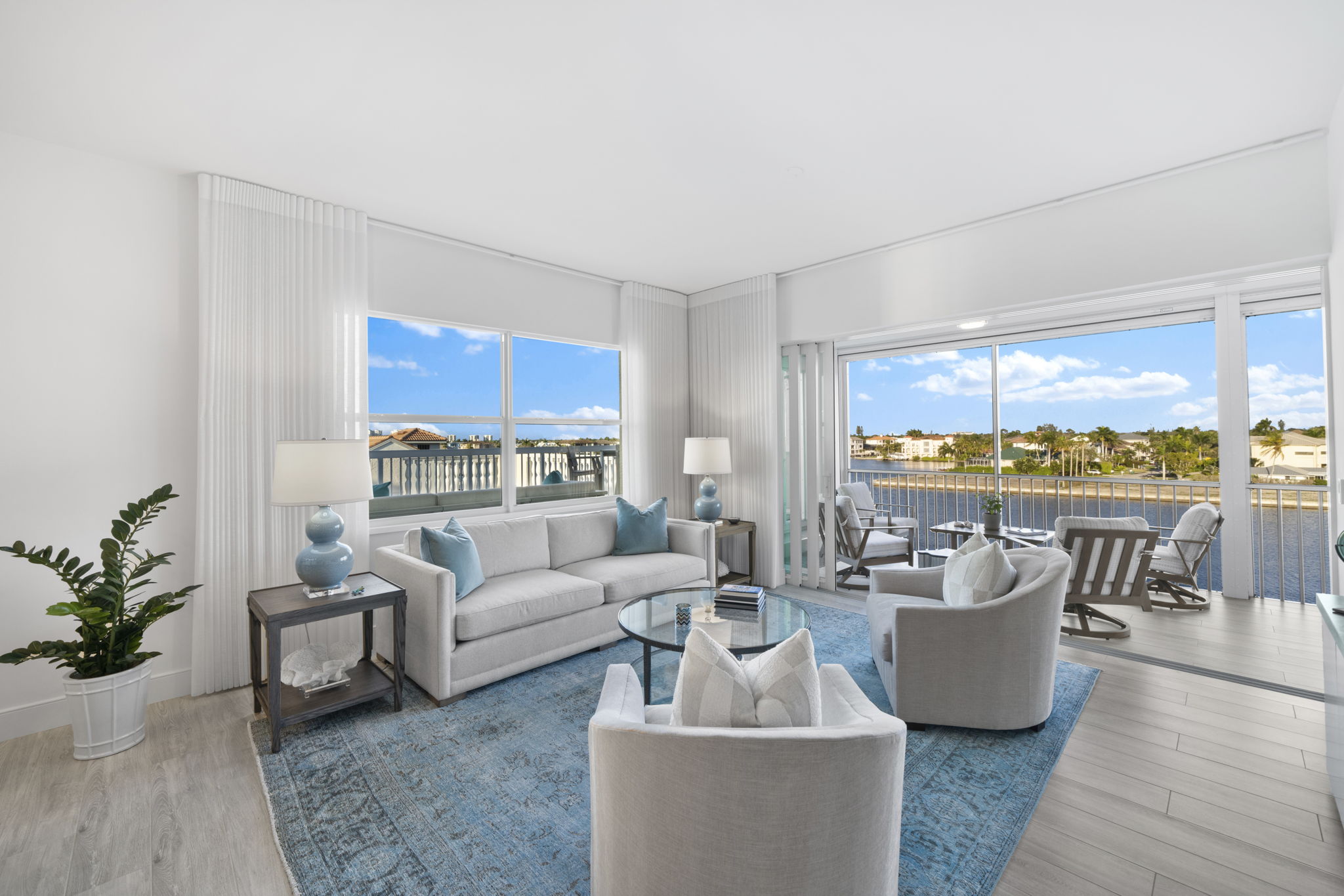 a condo living room with white furniture, a blue carpet, and windows surrounding the room looking out over the water