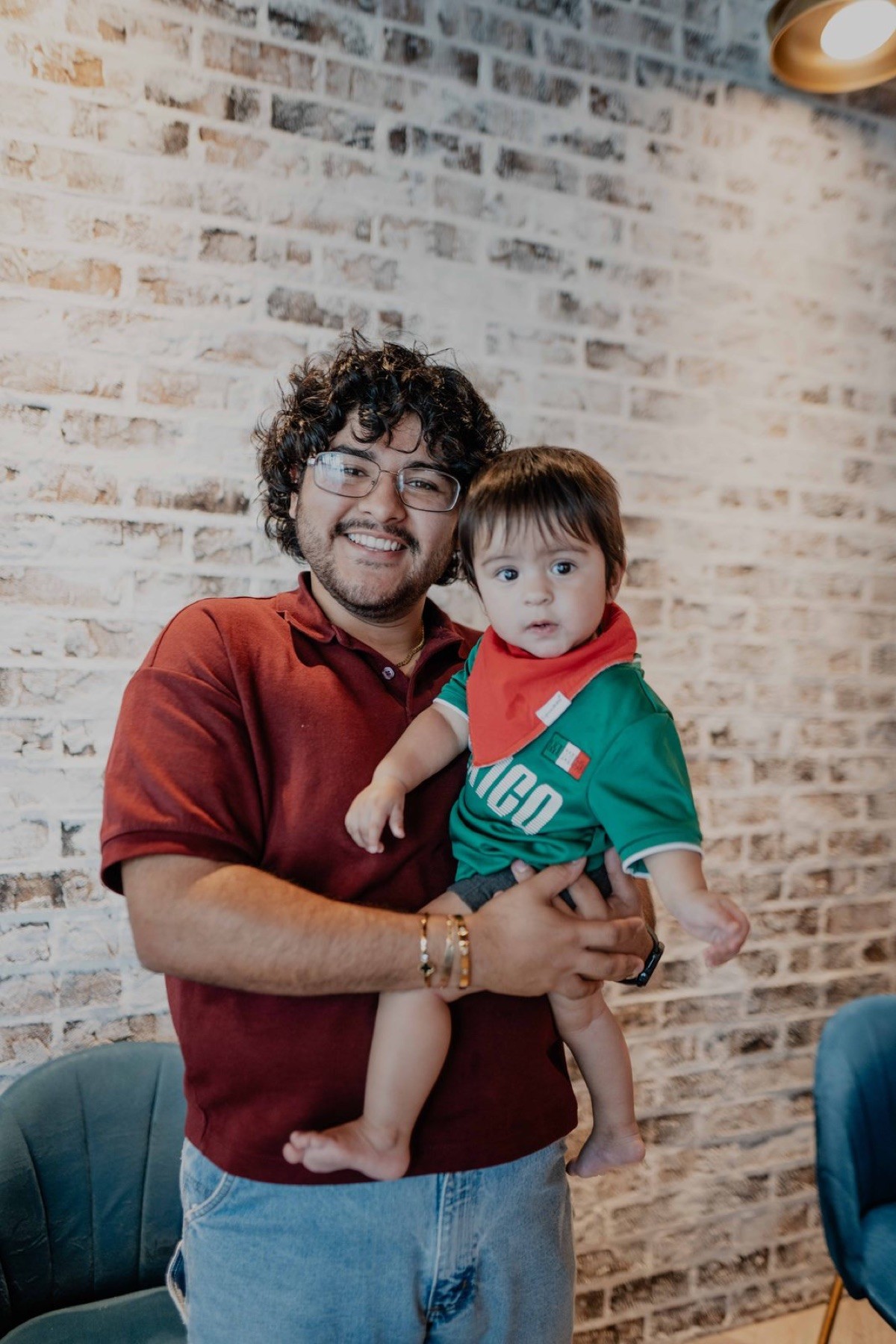 Young dad holding his baby in front of a white brick wall