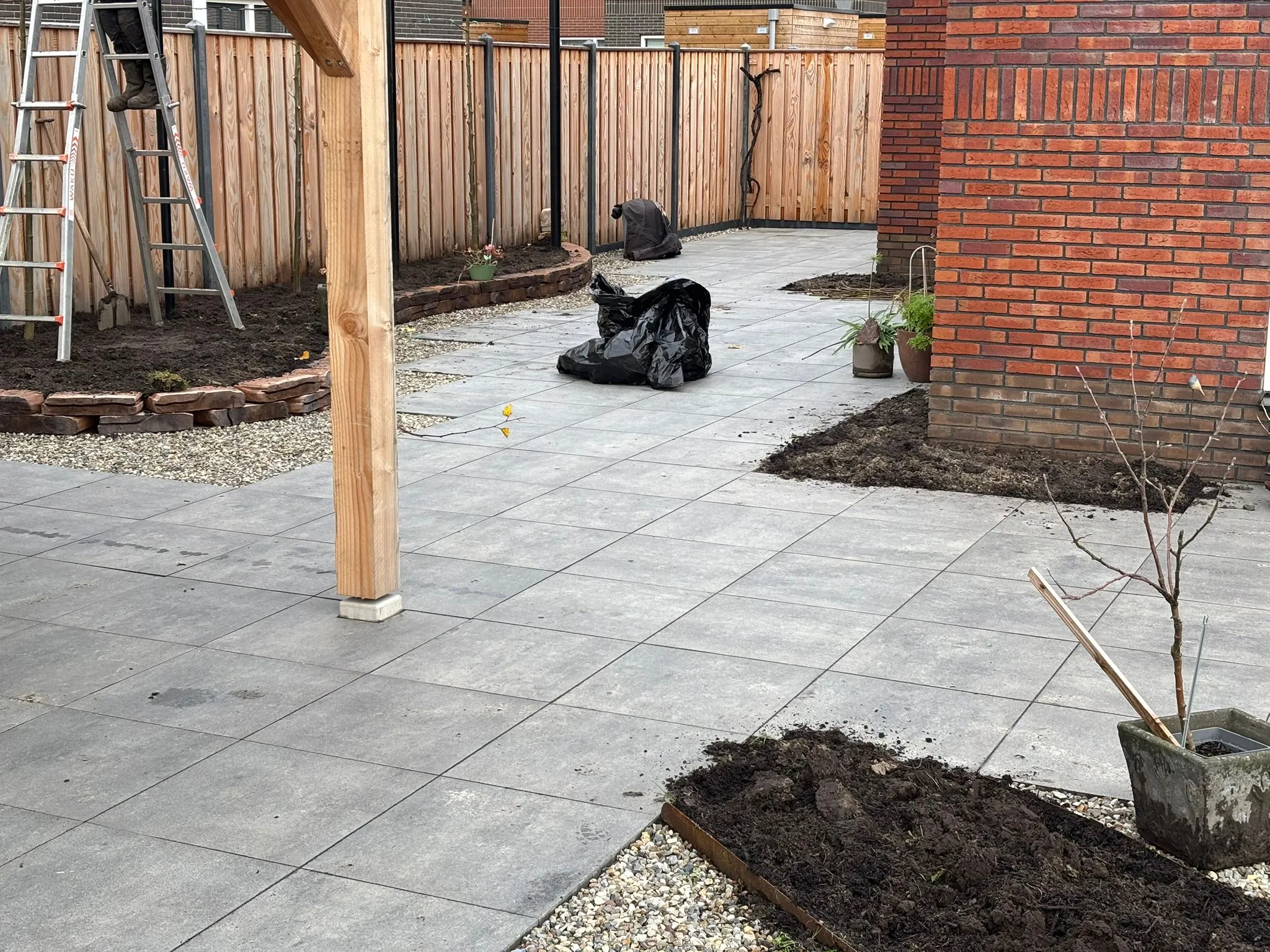 Strak betegeld tuinpad met grindranden, jonge planten en houten pergola in aanleg bij vrijstaande woning in Gorredijk.