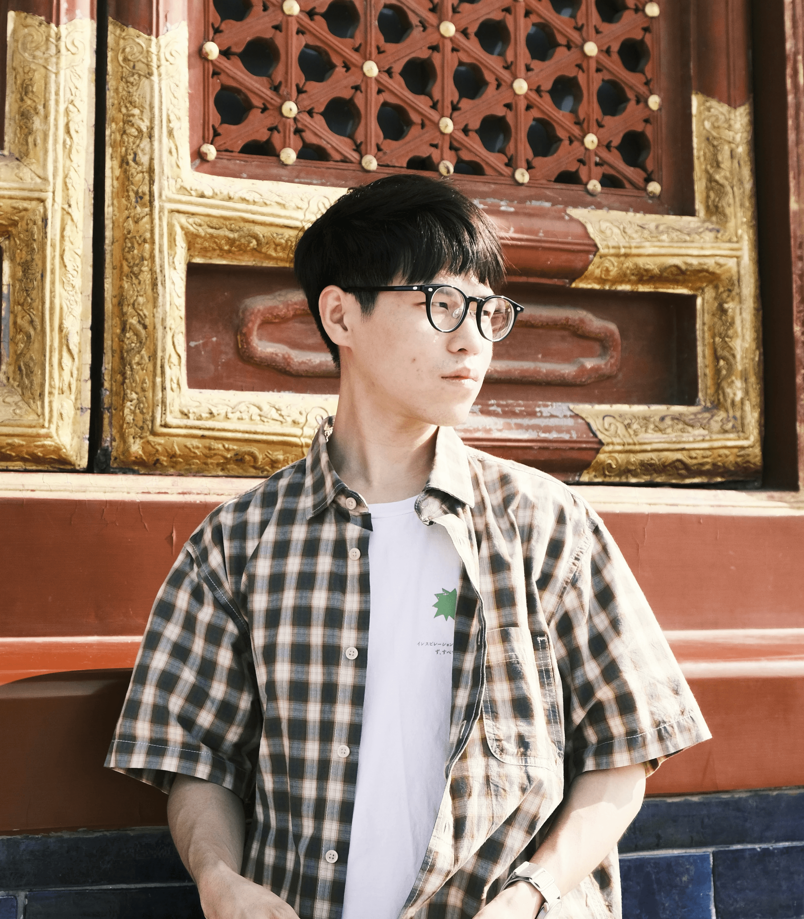 Young man in glasses stands by ornate wooden doors.