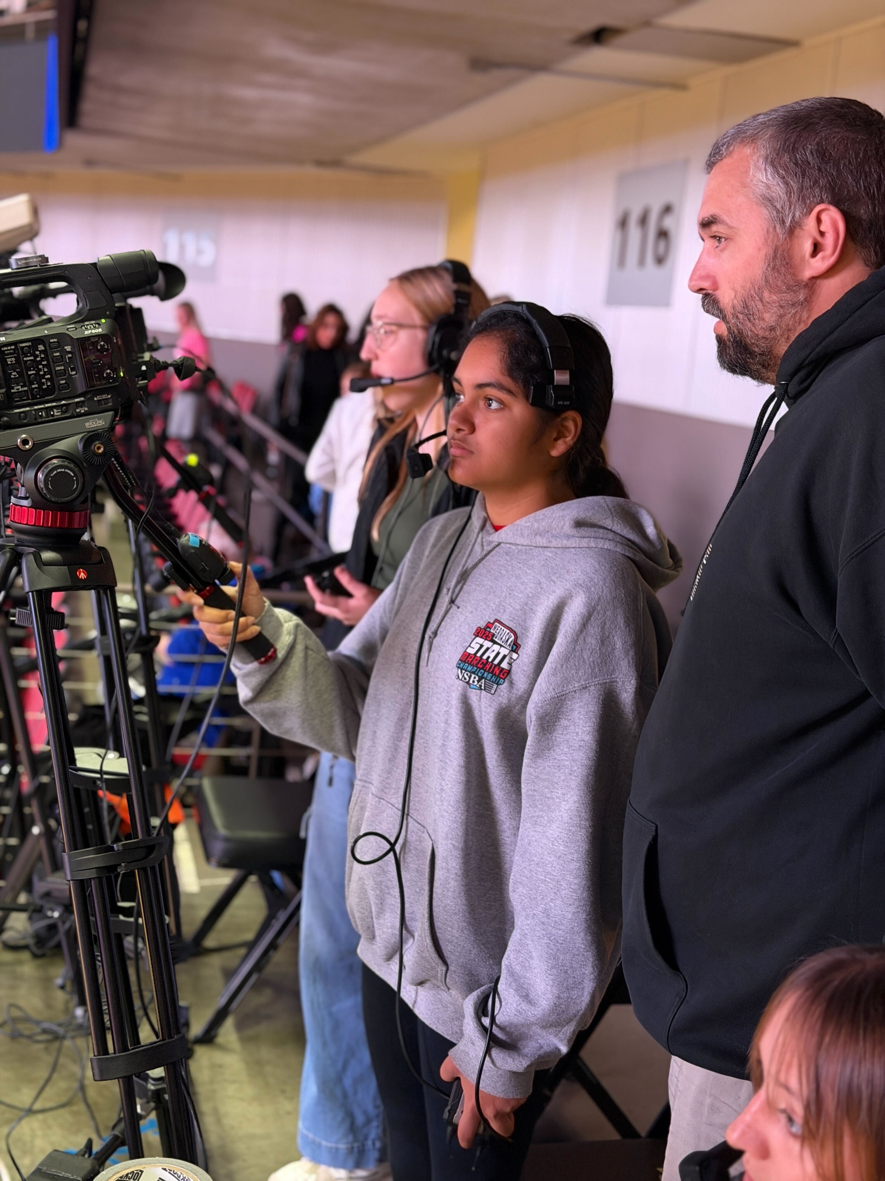 Student broadcast crew with headsets operating cameras at a state wrestling tournament alongside their teacher