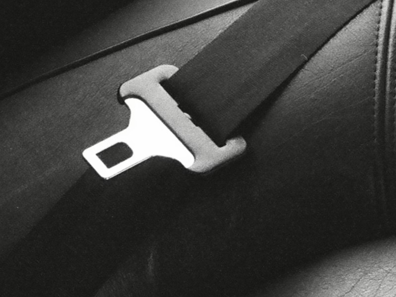 Close-up of a metal seatbelt buckle on a black seat, emphasizing safety in vehicles.