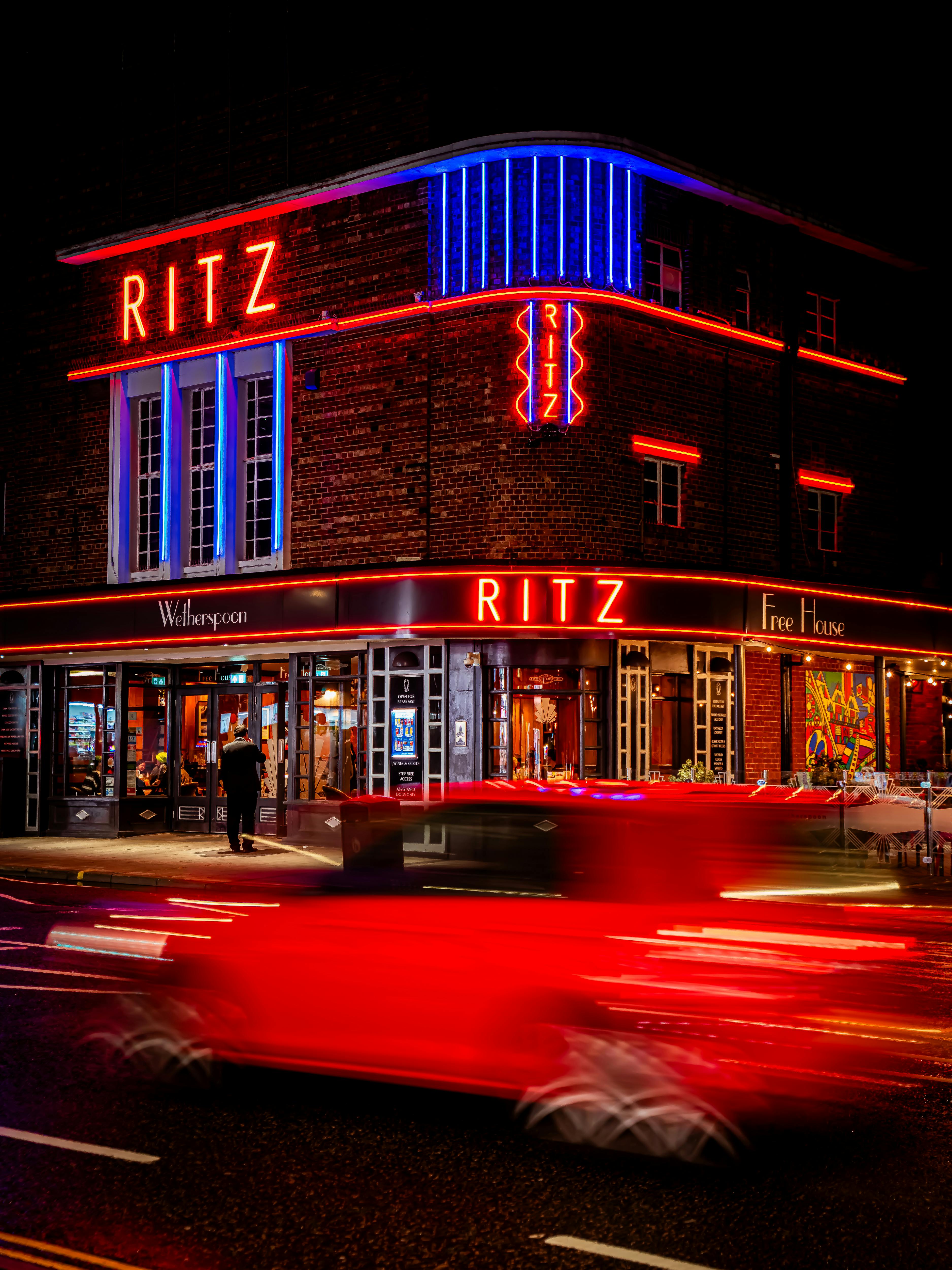 RITZ 霓虹招牌與紅色車流光軌，展現城市夜生活的動態模糊視覺