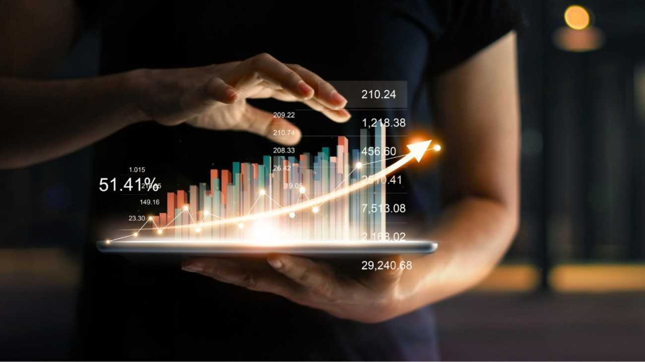 A person holding a laptop with a virtual image f a bar graph showing increases with his other hand hovering overon