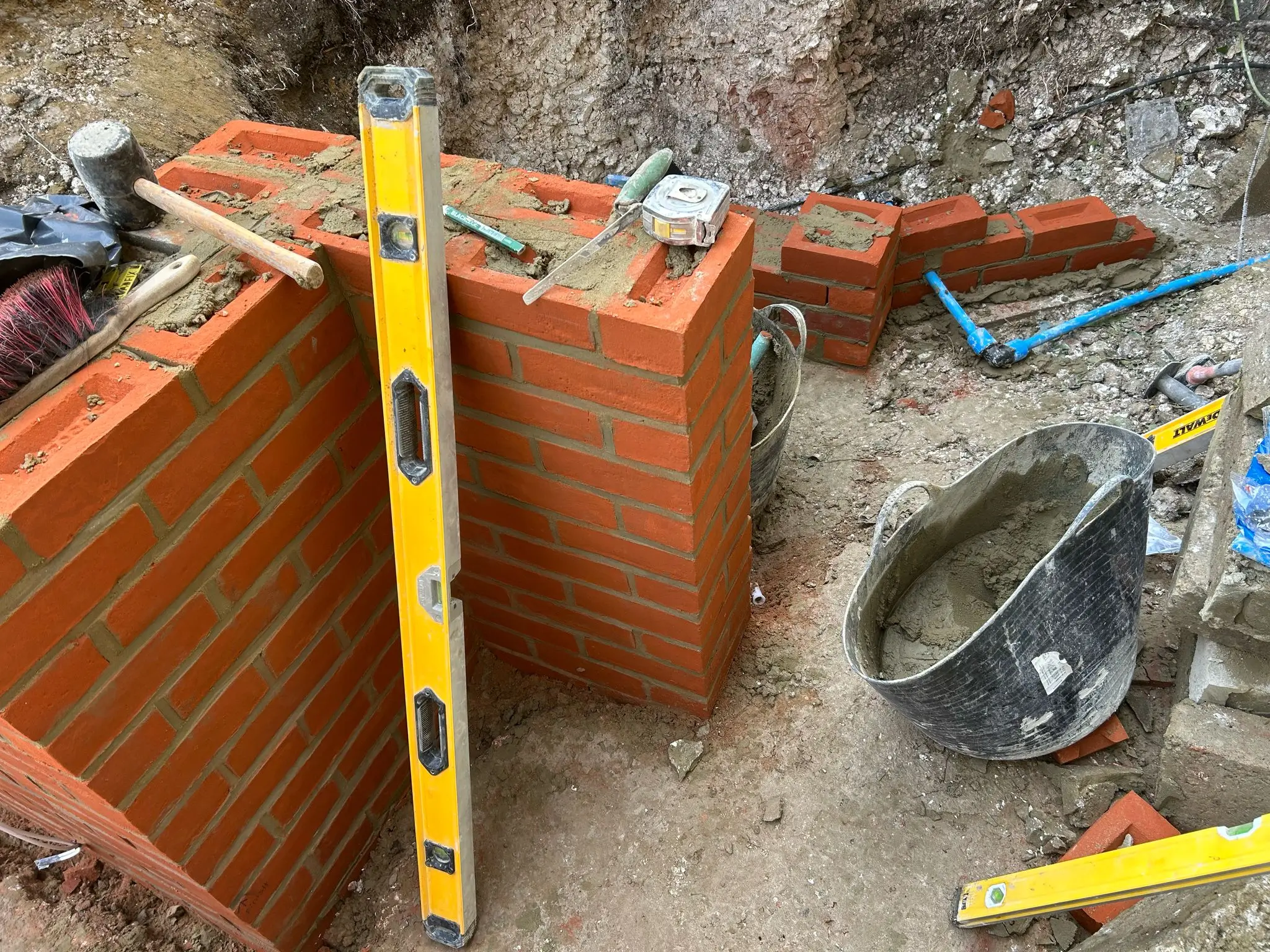 Construction site with orange bricks stacked, a yellow level nearby, and tools scattered on the ground.