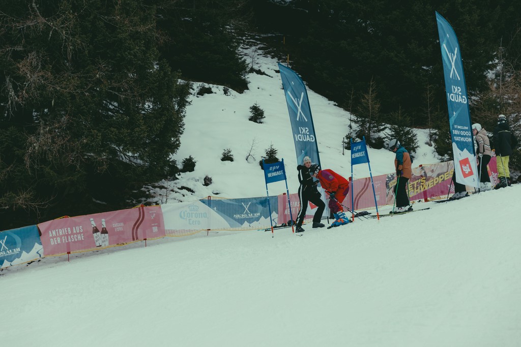 Skiers preparing on snowy slope with trees and banners in winter landscape.