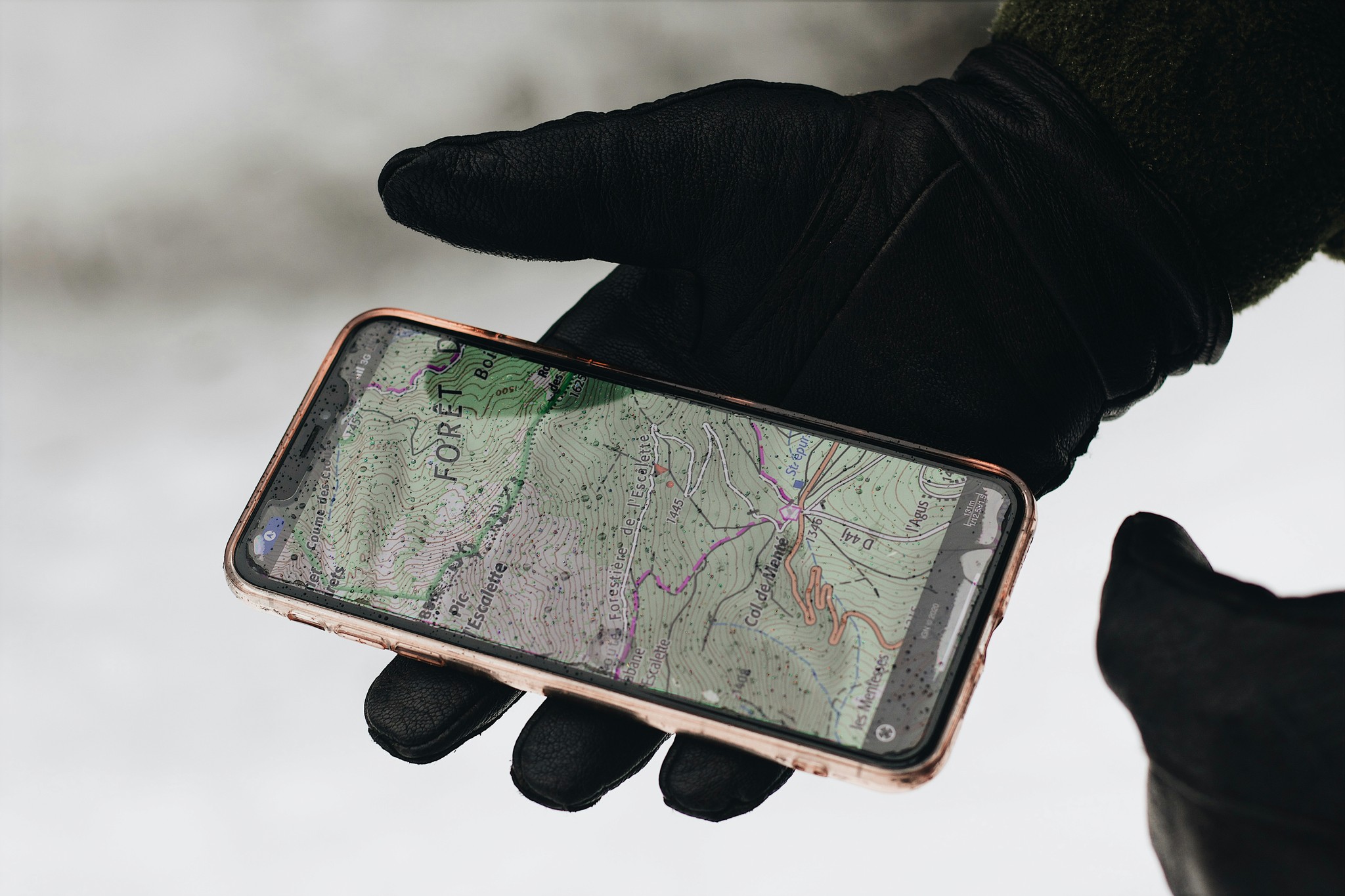 Gloved hand holding a smartphone displaying a detailed topographic map app, ideal for navigation and hiking in outdoor environments.