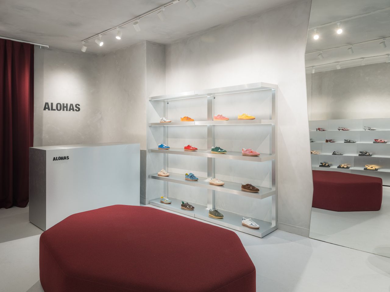 Interior of the Alohas New York retail store featuring a minimalist reception desk with logo signage, soft plaster walls, and open shelving displaying footwear.