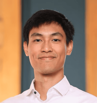 A person with wavy light hair stands facing slightly to the left, wearing a striped shirt against a neutral background.