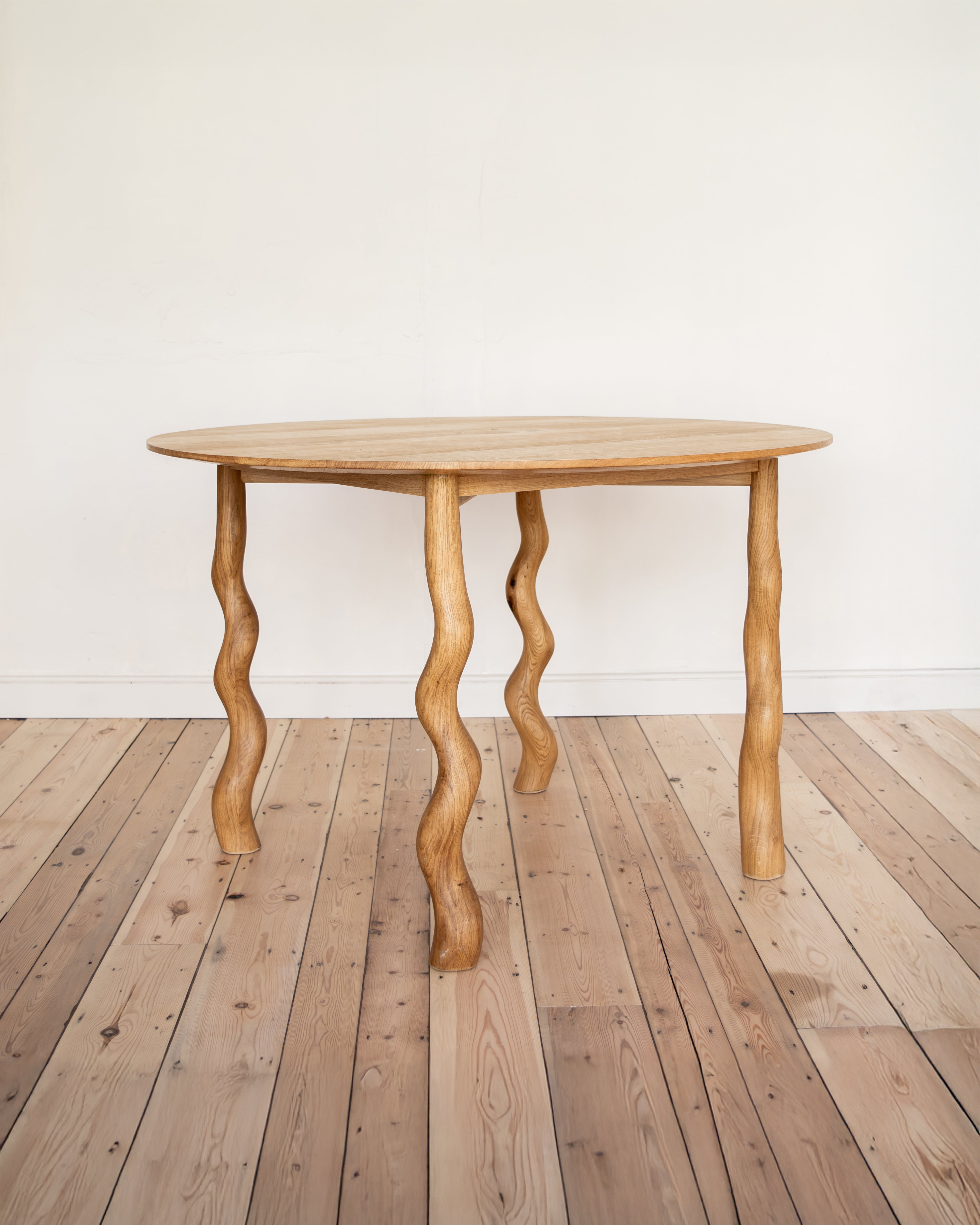 Wooden table with wavy legs on a wooden floor against a white wall
