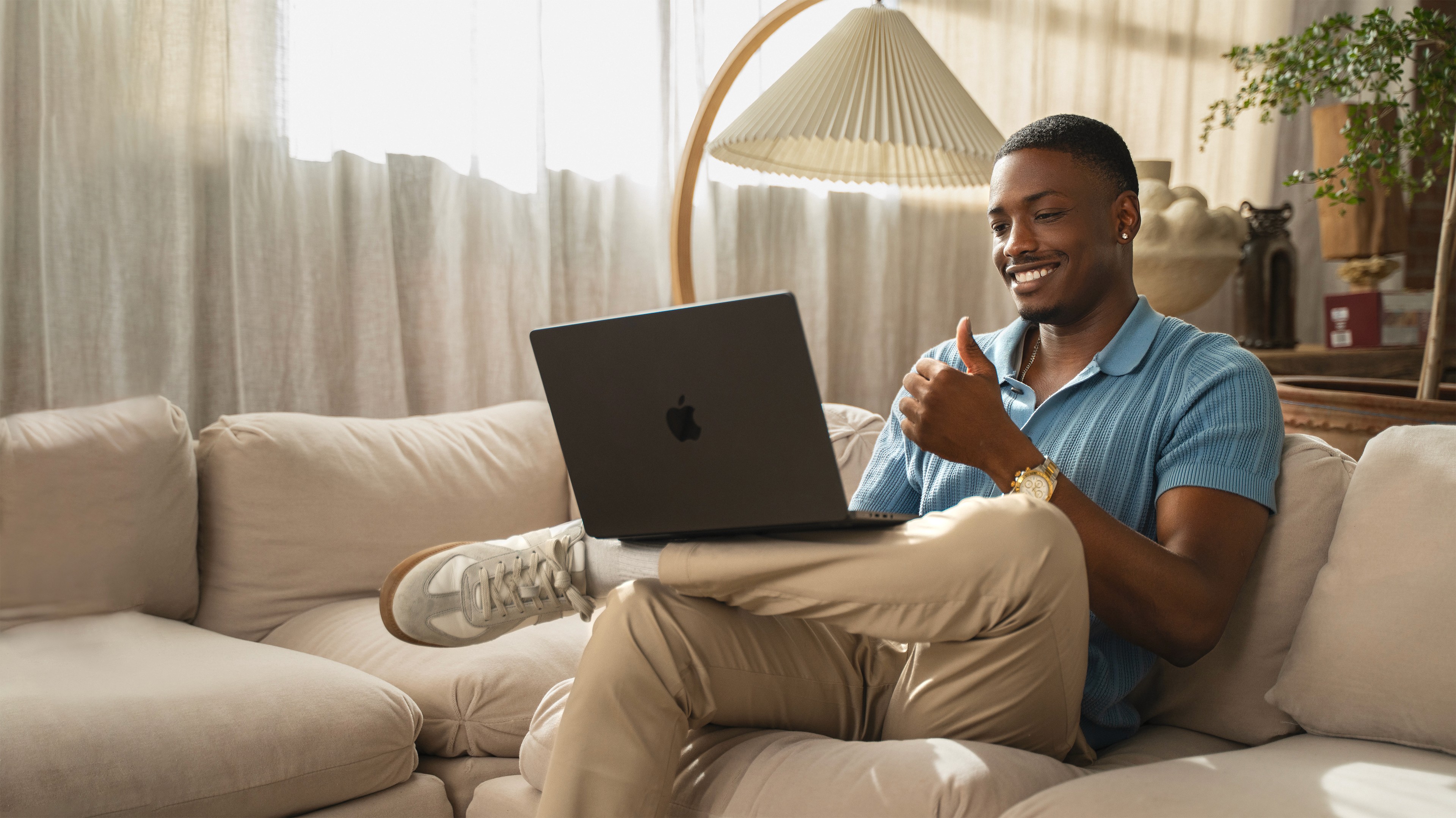 Young African American professional in late 20s watching UNBLOKD CO free coaching resources on laptop, seated on a beige sofa in a Japandi minimalist loft, dressed smart casual, smiling while learning Clarity, Alignment and inner leadership online.