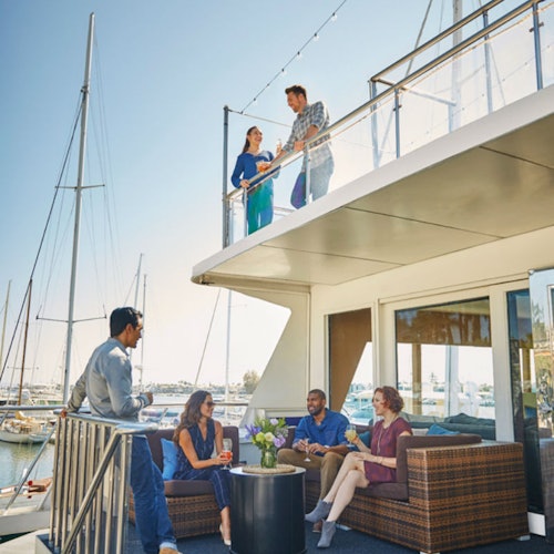 人们正在船上放松。两个人在上层甲板的栏杆旁,四个人围坐在下层甲板的一张小桌子旁。