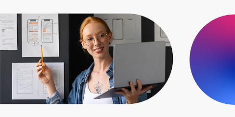 UX Design course blog showing a woman presenting UX wireframes on a wall while holding a laptop, illustrating UX design planning, prototyping and digital product design.