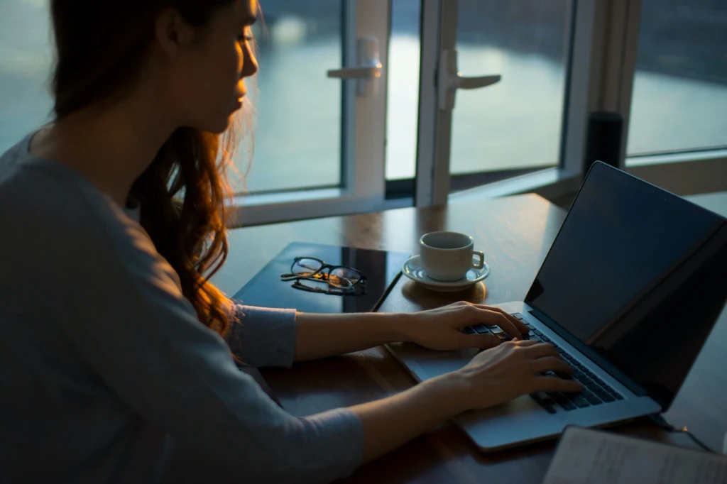 Professional working on laptop with coffee and glasses at desk in evening