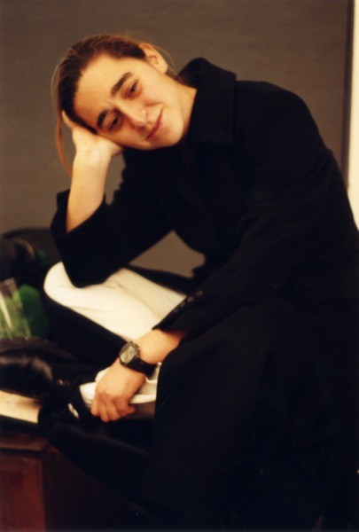 A photo of a man wearing a black dress and white pants, while leaning his head on a hand.