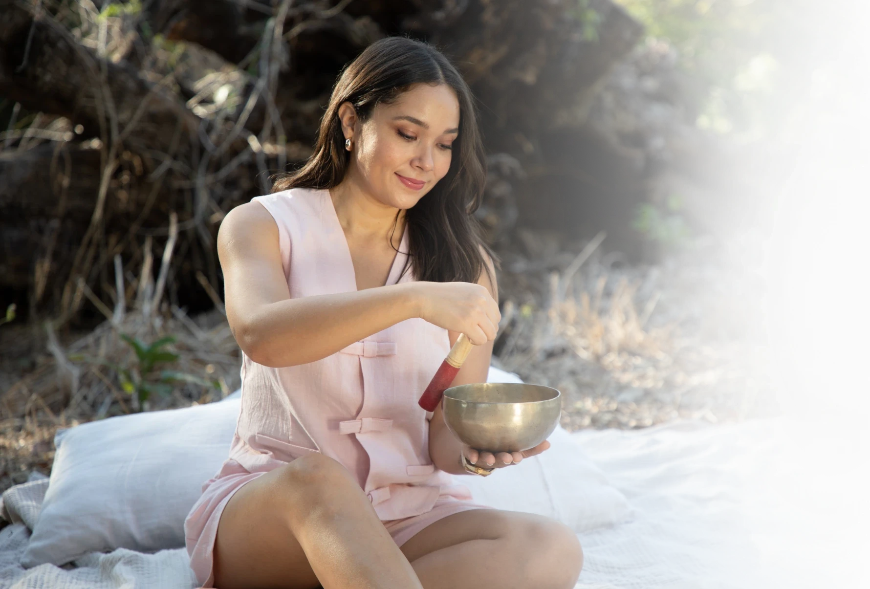 Minerva Alvarez, terapeuta holística, sonriendo mientras usa un cuenco tibetano en un entorno natural.