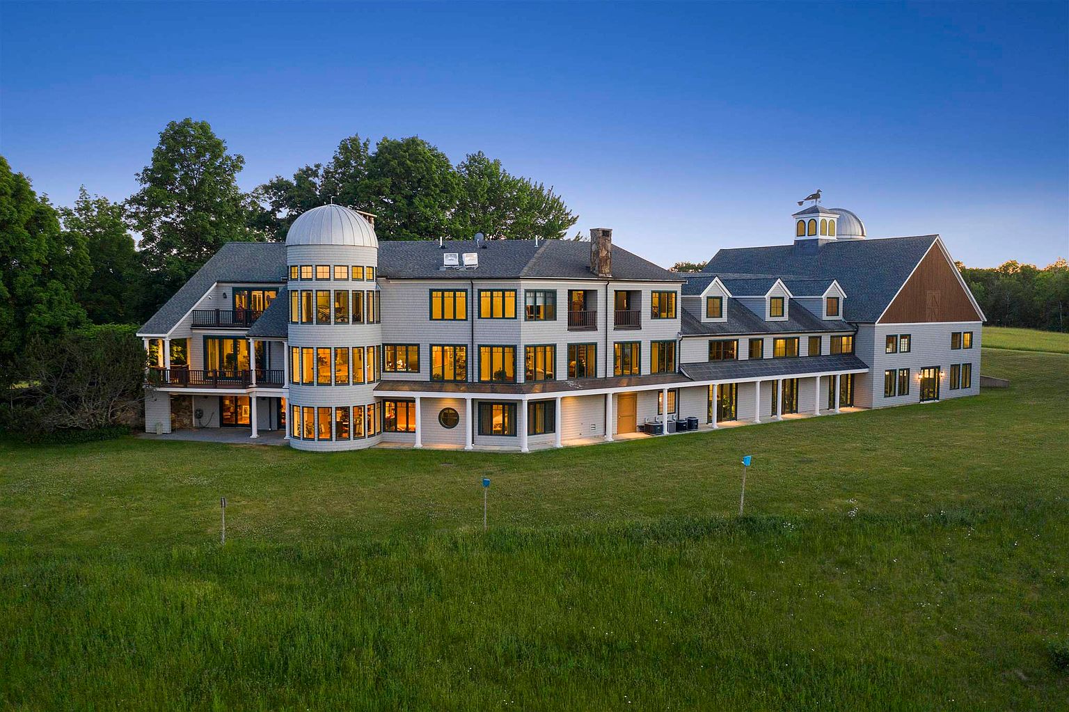 Sunset view of Meadow View Manor in Barrington, NH, a sprawling 17,000 sq. ft. luxury estate with large windows and turreted architecture, ideal for high-end Airbnb stays and private events.