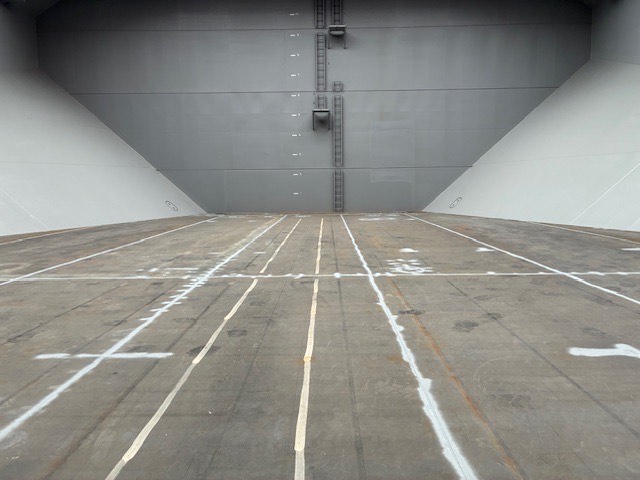 A clean and empty cargo hold of a bulk carrier prepared for loading, showing a clear steel floor and structural walls.