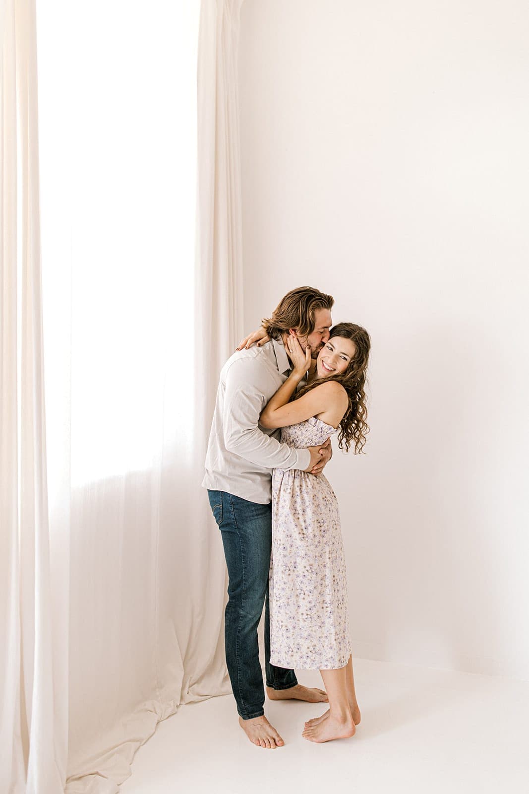 The couple laughs while embracing next to a window, bathed in natural light at Revelator Studio in Shreveport.