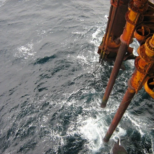 Rostige Metallrohre, die von einer Struktur mit sichtbaren Bolzen in das unruhige Meerwasser ragen.